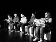Fünf Personen sitzen in einer Reihe und lesen Zeitung